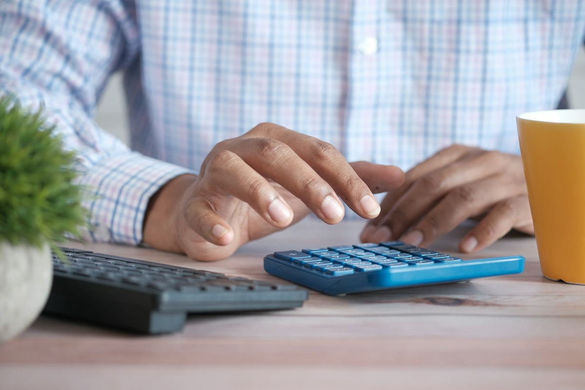 Person using a calculator at a desk with a coffee mug